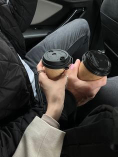 a person holding a cup in their hand while sitting on the back seat of a car