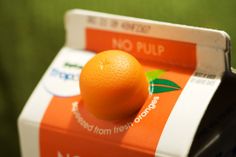 an orange sitting on top of a carton of nourishment juices