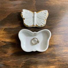 two white and gold butterfly shaped dishes on top of a wooden table next to each other