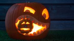 a carved pumpkin sitting in the grass with an evil face on it's side