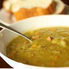 a white bowl filled with soup next to a piece of bread on a plate and spoon