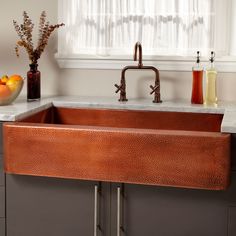 a large copper sink in a kitchen with marble counter tops and brown cabinets, along with vases filled with flowers