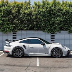 a white porsche gtr parked in a parking lot next to a wall with hedges