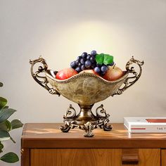 a gold bowl filled with fruit sitting on top of a wooden table next to a book