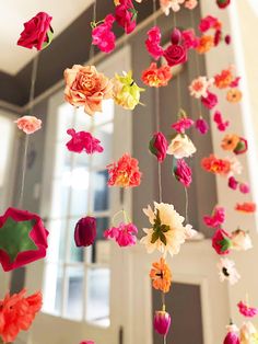 colorful paper flowers hanging from strings in front of a door with windows behind them and an open window