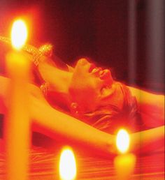 a woman laying on top of a bed next to candles in front of her face