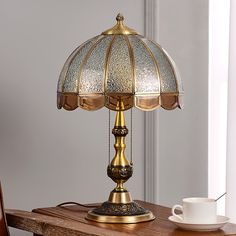 a table lamp sitting on top of a wooden table next to a cup and saucer