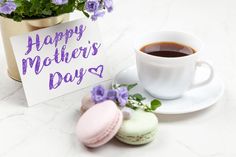 a cup of coffee and two macaroons on a table with a happy mother's day card