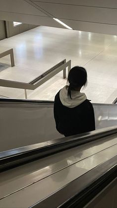 a woman riding down an escalator with her back turned to the camera,