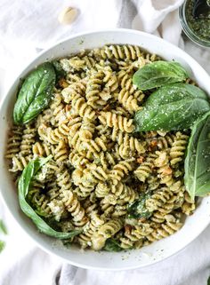 a white bowl filled with pasta and spinach on top of a table next to some sauce