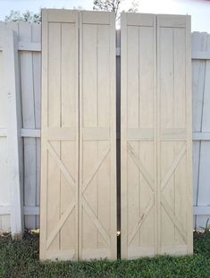 two wooden doors sitting next to each other in the grass near a white picket fence