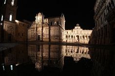 an old building is lit up at night with its reflection in the water on the ground