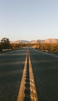 an empty road in the middle of nowhere, with mountains in the backgroud