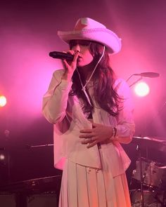 a woman in a white dress and hat singing into a microphone