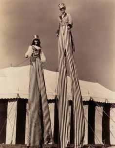 two women standing on top of a tent in front of a white building with black and white stripes