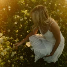 a woman kneeling down in a field of flowers