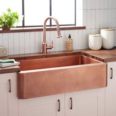 a copper sink in a kitchen with white cabinets