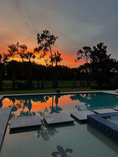 the sun is setting over a swimming pool with lounge chairs and trees in the background