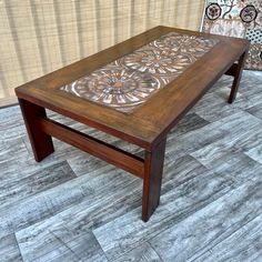 a wooden table sitting on top of a tile floor next to a wall with an intricate design