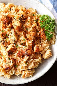 a white bowl filled with rice and meat covered in parsley on top of a wooden table