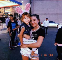 two girls in bunny ears are hugging each other on the street while people walk by