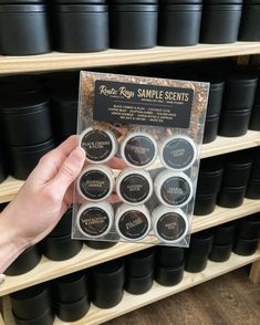 a person holding up a package of sample items in front of shelves with black cups