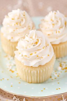 three cupcakes with white frosting and sprinkles on a plate