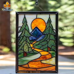 a stained glass window with trees and mountains in the background, hanging on a chain