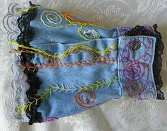 an old pair of blue jeans with embroidered flowers and leaves on them sitting on a white lace tablecloth