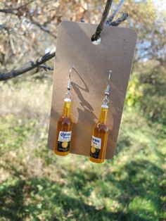 two bottles of beer hanging from a tree branch in front of some grass and trees