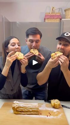 three people sitting at a table eating sandwiches and making faces with the camera man in the background