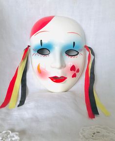 a white mask with red, yellow and blue stripes around it's face on a white surface