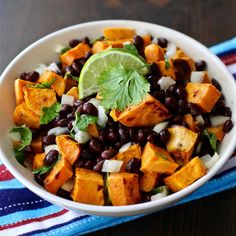 a white bowl filled with black beans and sweet potato salad on top of a colorful towel