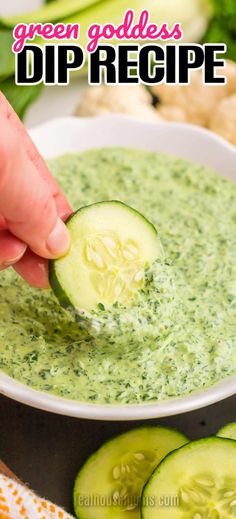 a hand dipping a cucumber into a bowl of green goddess dip recipe with sliced cucumbers in the background