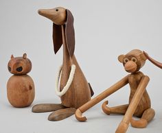 three wooden toy animals sitting next to each other on a white surface with one holding the tail of another animal