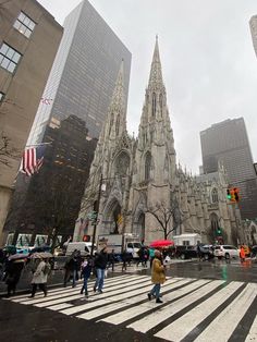 people are crossing the street in front of a large cathedral with tall buildings on both sides