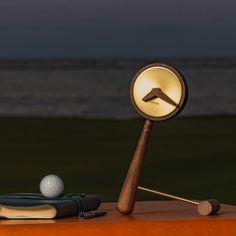 a golf ball is sitting on top of a wooden table next to a lamp and book