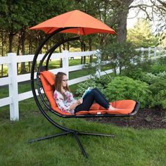 a woman is sitting in an orange swing chair with her laptop on the ground next to a white picket fence