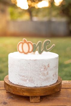 a white cake topped with a wooden one and two pumpkins on top of it