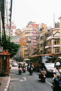 many people are riding motorcycles down the street in front of some buildings and signs on the side of the road