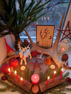 a table topped with candles and deer antlers on top of a wooden tray next to a window