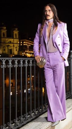 a woman in purple is standing on a balcony with her hands behind her back and looking at the camera