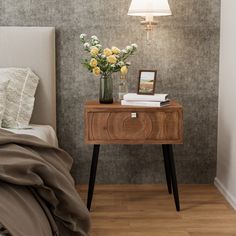 a bedside table with flowers on it next to a lamp and a bed in a room