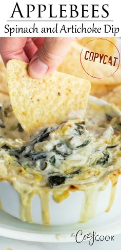 a hand dipping a tortilla chip into a bowl of spinach and artichoke dip