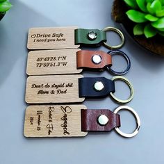 four wooden keychains with engraved names and date on them, sitting next to a potted plant