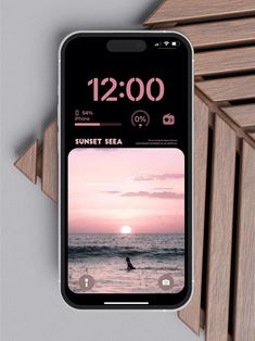 an iphone with the sun set sea on it's screen next to some wooden slats