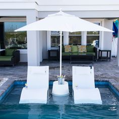 two lawn chairs and an umbrella in the middle of a pool with lounge chairs around it