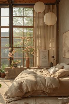 an unmade bed in front of two large windows with flowers on the floor and hanging lanterns above it