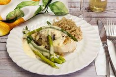 a white plate topped with fish covered in gravy next to rice and asparagus