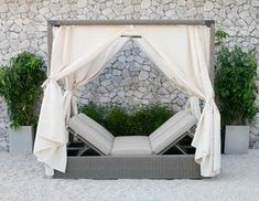 a bed sitting next to a stone wall covered in white sheets and draping